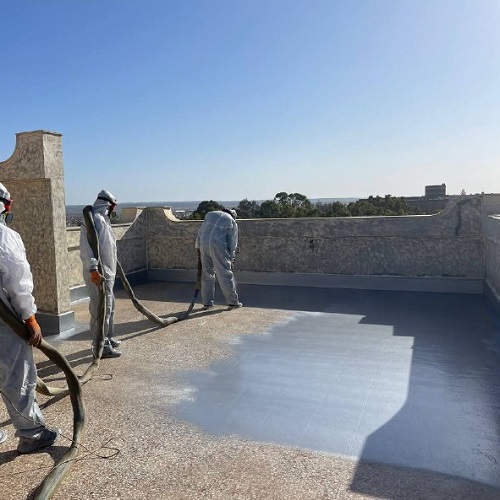عمال يطبقون مادة البولي يوريا على سطح مبنى.