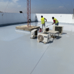 تطبيق مادة بولي يوريا باردة بواسطة فني باستخدام رول على سطح مبنى يحتوي على وحدات تكييف هوائي.