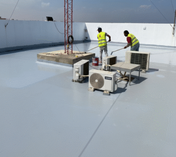 تطبيق مادة بولي يوريا باردة بواسطة فني باستخدام رول على سطح مبنى يحتوي على وحدات تكييف هوائي.